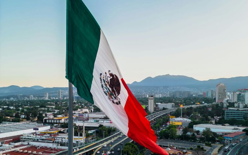 Bandera de México ondeando sobre la Ciudad de México al atardecer, símbolo del país protagonista en el documental Depeche Mode: M.