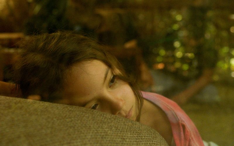 Fotograma de la película Tótem de Lila Avilés, con una niña recostada mirando a través de la luz cálida de una casa