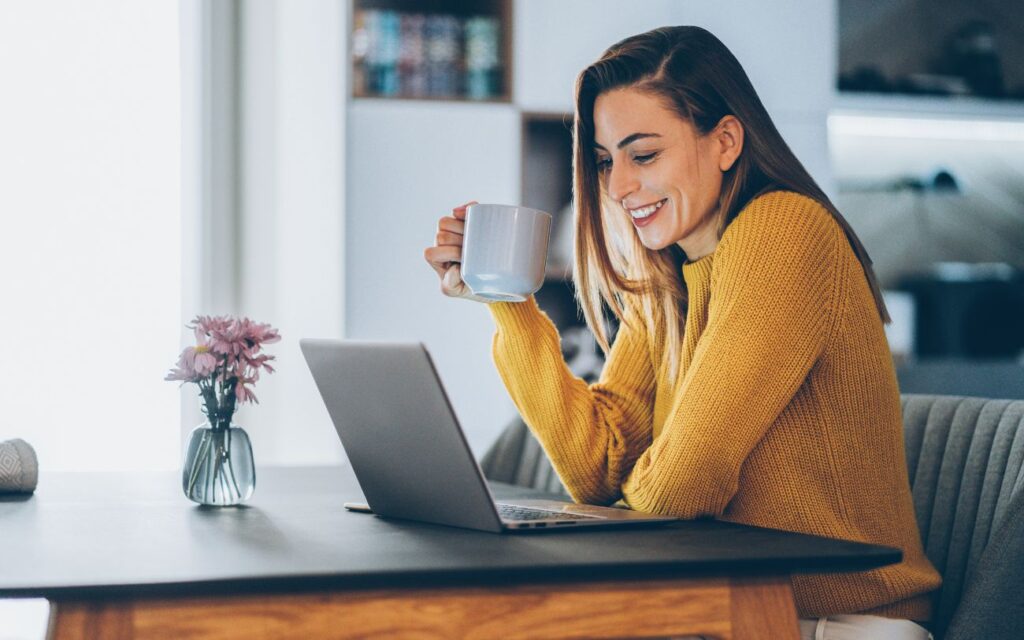 Mujer trabajando desde casa con su laptop y taza de café, representando el equilibrio del trabajo remoto.