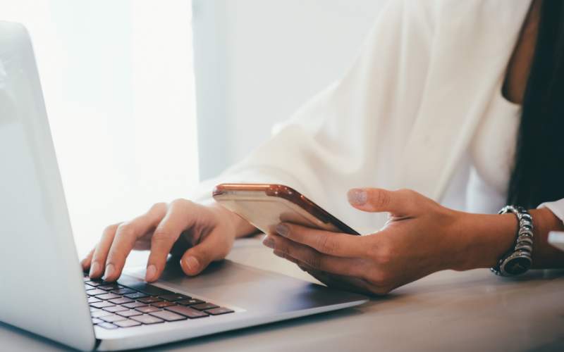 Persona trabajando desde casa mientras usa una laptop y un teléfono para compartir archivos y recursos en línea.