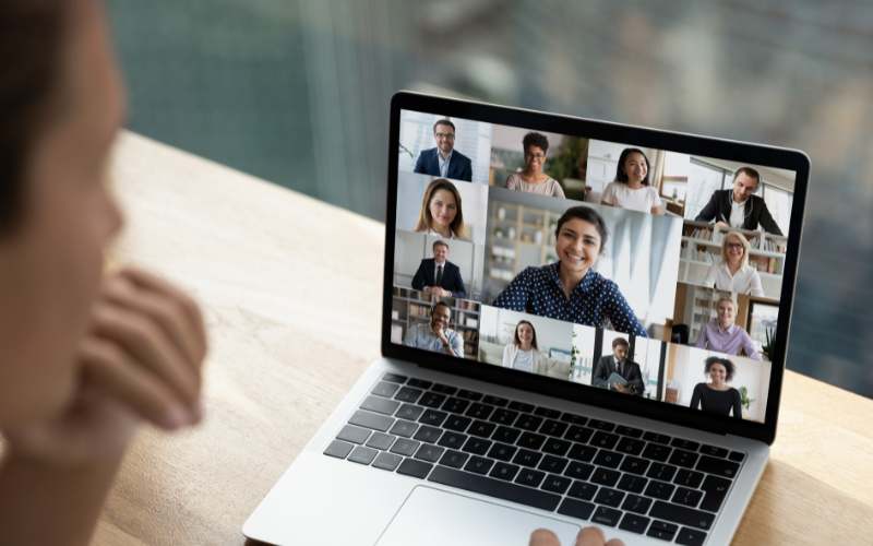 Persona participando en una videollamada grupal desde su laptop, mostrando a varios compañeros de trabajo conectados.
