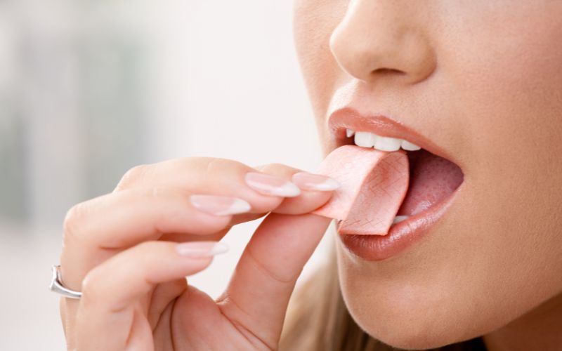 Mujer masticando chicle, una técnica recomendada por estudios para ayudar a eliminar canciones repetitivas de la mente.