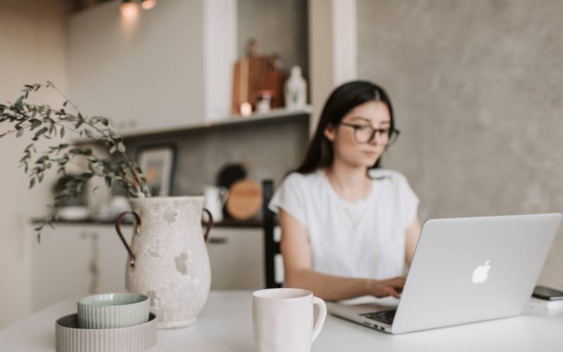 Mujer trabajando desde casa con su laptop en una mesa, disfrutando las ventajas del trabajo remoto.