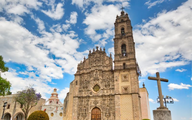 Fachada barroca del templo de San Francisco Javier en Tepotzotlán bajo un cielo azul con nubes.
