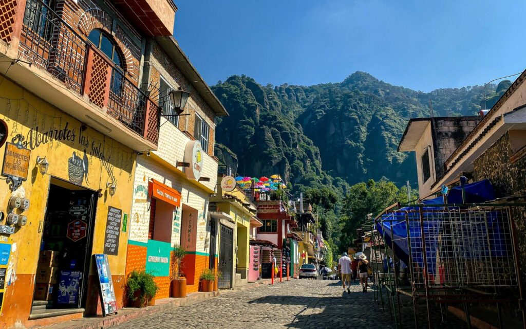 Calle empedrada de Tepoztlán con casas coloridas, tiendas locales y montañas verdes del Tepozteco al fondo.