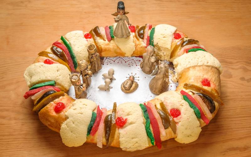 Rosca de Reyes tradicional mexicana con frutas cristalizadas y figuras del nacimiento colocadas al centro sobre una mesa de madera.